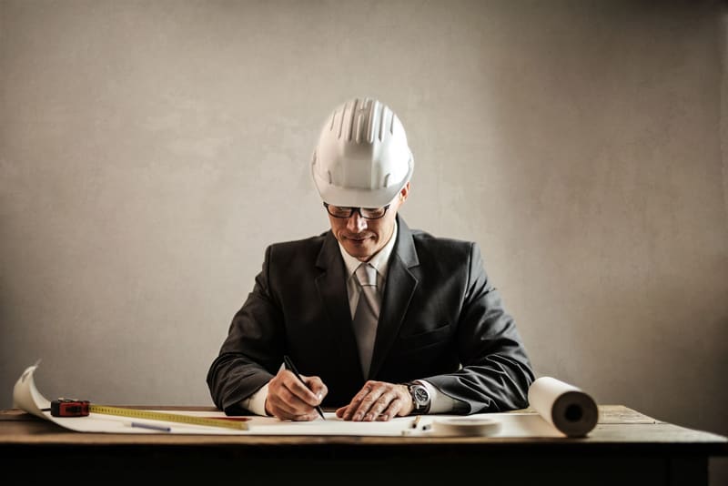 Mann mit Bauhelm unterschreibt Unterlagen am Schreibtisch